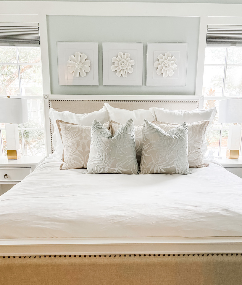 Primary bedroom with upholstered bed and trio of white floral art panels