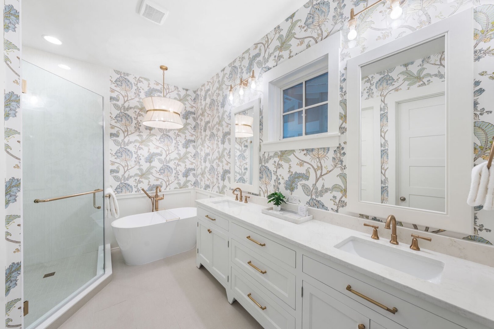 Primary bath with floral wallpaper, freestanding tub, and brass fixtures