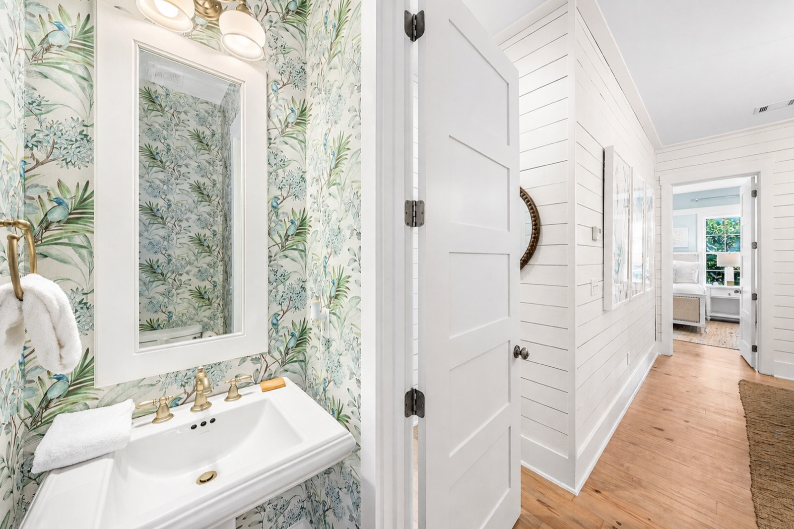 Powder room with palm-print wallpaper and white shiplap hallway beyond